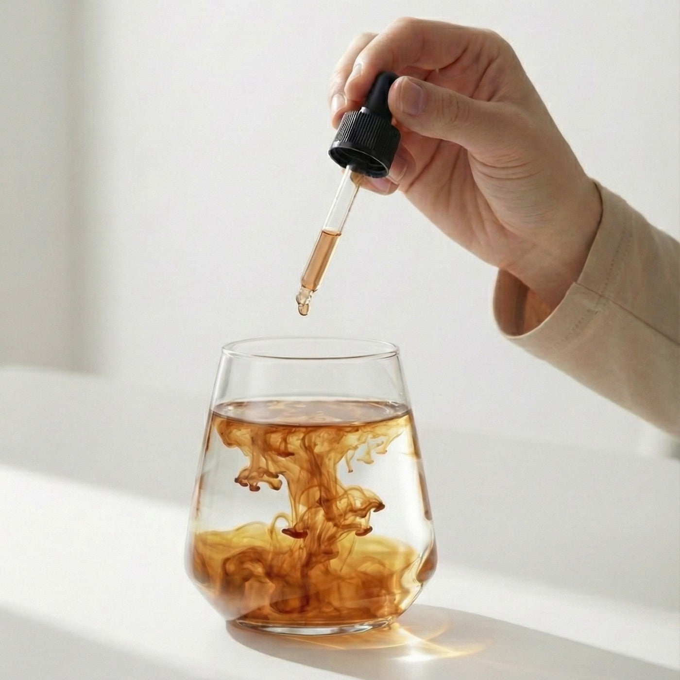 Hand dropping Polyextract mushroom extract into a glass with a white background