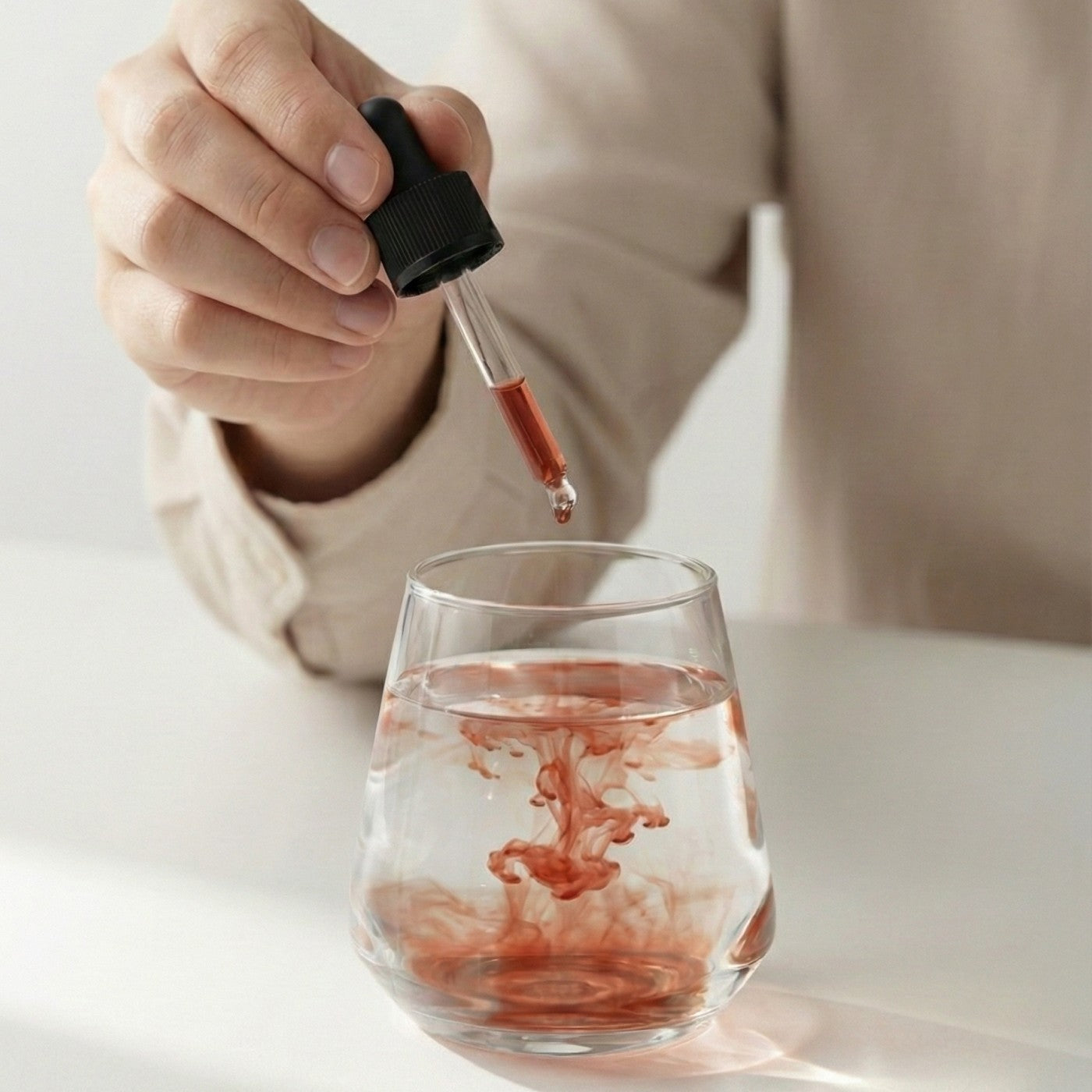 Hand using a dropper to add red Polyextract mushroom supplement into a glass of water on a light background